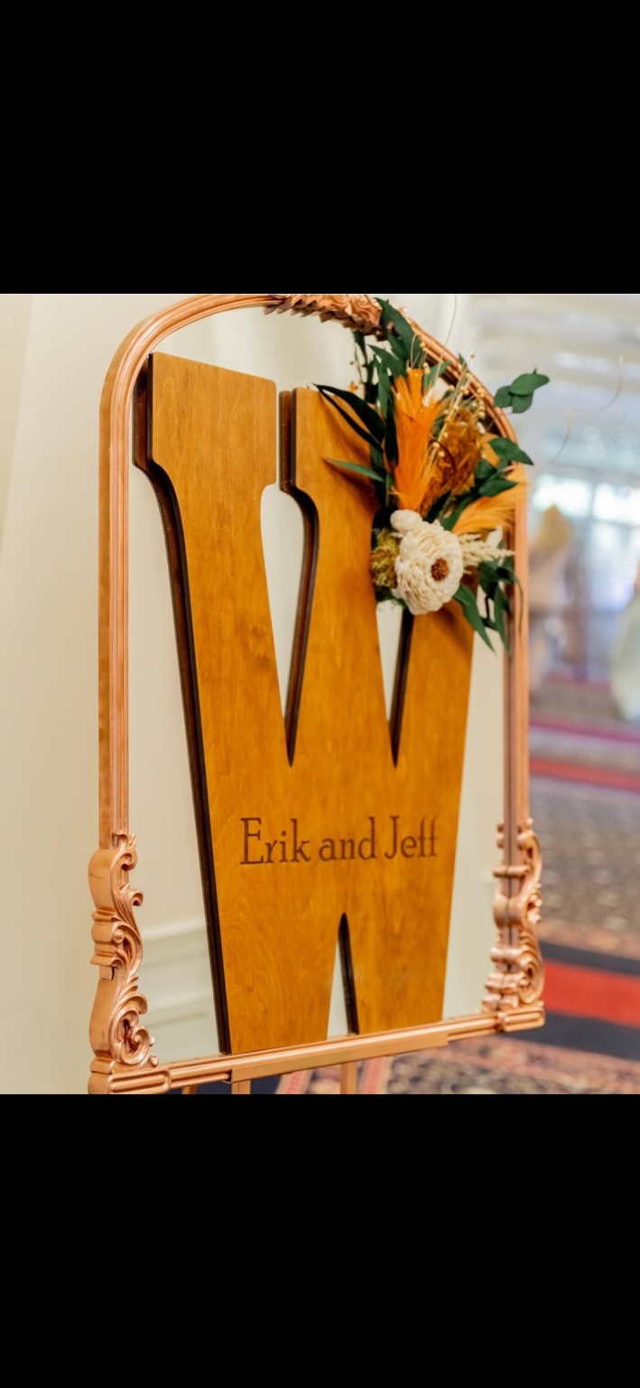 Personalized wooden W sign for Erik and Jeff displayed in an ornate rose-gold mirror frame with florals